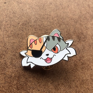 May include: A white, gray, and orange enamel pin of a cat with an eyepatch. The cat has a mischievous expression and a single red eye.