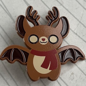 May include: A brown bat with reindeer antlers and a red scarf. The bat has large, white eyes and a small, pink nose. The bat is wearing a red scarf around its neck.
