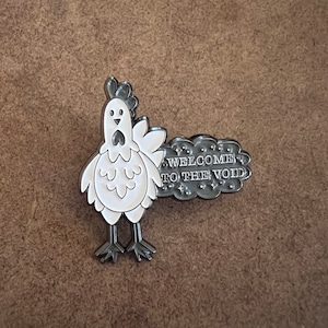 May include: A white enamel pin featuring a cartoon chicken with the text "Welcome to the Void" on a black cloud.