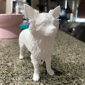 May include: A white, 3D-printed Chihuahua figurine. The dog is standing with its head up, ears perked, and fur detailed. The figurine is made of a solid white material and is a decorative item.