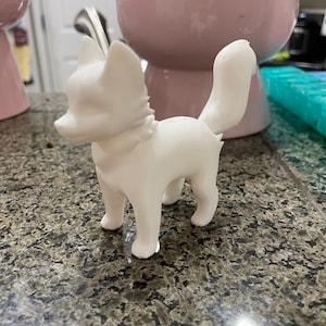 May include: A white ceramic figurine of a fox standing on a granite countertop. The fox has a long, bushy tail and a pointed snout.