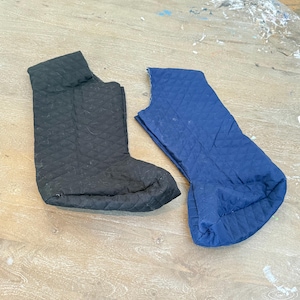 May include: Two quilted fabric boot covers, one black and one blue, are displayed on a wooden surface. The black boot cover is fully assembled, while the blue one is partially constructed. Both have a diamond pattern.