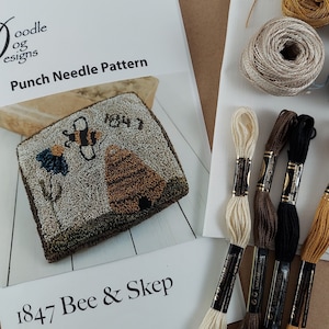 May include: A craft kit with a "Doodle og Designs" punch needle pattern titled "Bee & Skep" featuring a bee and beehive design. Includes embroidery floss in various colors and spools of yarn. The kit is for a craft project.
