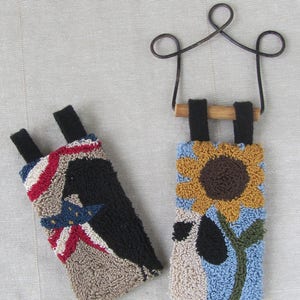 May include: Two hand-stitched phone cases. One has a patriotic design with red, white, and blue stripes and a star. The other features a sunflower against a blue and beige background. Both have black straps.