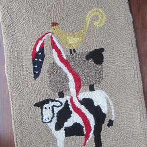 May include: A hand-hooked rug featuring a cow, sheep, and chicken stacked on top of each other. The chicken holds a red, white, and blue design. The rug has a tan background and a textured appearance.