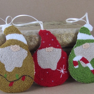 May include: Three handmade Christmas gnome ornaments. One is gold with a white beard and hat, and a string of lights. The second is red with a white beard and hat, and a snowflake. The third is green with a white beard and hat, and a candy cane.