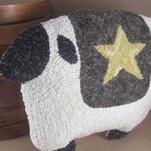 May include: Handmade sheep-shaped rug with a star design. The rug features a white body, a dark gray back with a yellow star, and black accents. The rug is made of textured material and has a three-dimensional shape.