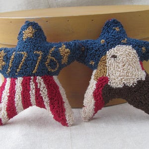 May include: Two star-shaped patriotic decorations. One star has red and white stripes, the other an eagle design. Both stars are connected by a blue section with gold stars and the number "1776".