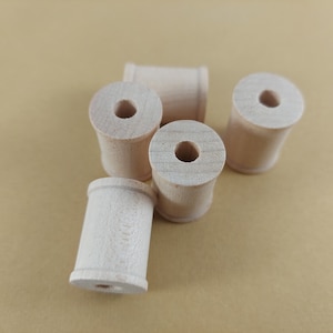 May include: A collection of unfinished wooden spools, ideal for crafts and DIY projects. The spools are cylindrical with a central hole, and are made of light-colored wood. They are arranged on a neutral background.
