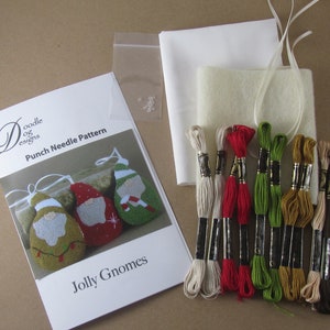 May include: A craft kit for punch needle embroidery featuring a "Jolly Gnomes" pattern. The kit includes embroidery floss in various colors, white fabric, a small bag of beads, and a pattern booklet. The booklet shows gnome designs in green, red, and gold.