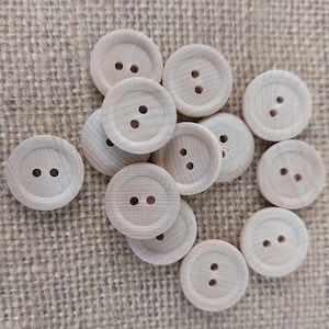 May include: A collection of round, light-colored wooden buttons, each featuring two central holes and a recessed circular design. These small, circular fasteners are crafted from natural wood and display a visible grain pattern across their surfaces.