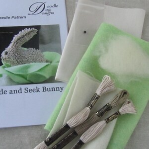 May include: A punch needle pattern kit for a "Hide and Seek Bunny" project. The kit includes a pattern, felt, embroidery floss, and other materials. The image shows a finished bunny nestled in a green felt leaf.