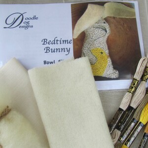May include: A craft kit labeled "Doodle Designs Bedtime Bunny" with a picture of a bunny. The kit includes cream-colored felt, embroidery floss in various shades of yellow, brown, and black, and stuffing.