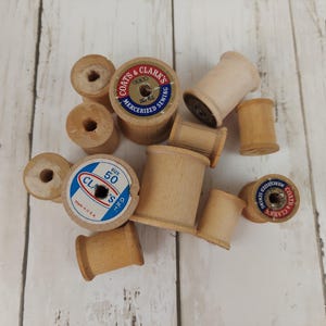 May include: A collection of light brown wooden sewing thread spools of varying sizes. Some spools feature circular paper labels with blue and red text reading Coats & Clark's Mercerized Sewing and Size 50 Clark's O.N.T. Made in U.S.A.