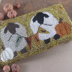 May include: A rectangular, hand-stitched rug featuring two stylized pumpkins with white, brown, and orange details against a yellow-green background. Small, decorative pumpkins surround the rug, suggesting a fall or harvest theme.