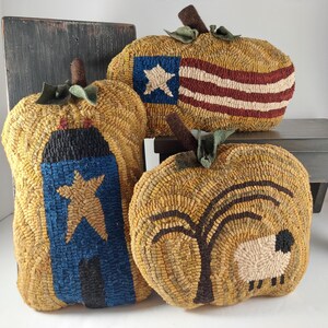 May include: Three decorative, handmade pumpkin-shaped pillows. One features a blue and gold star design, another a red and white striped flag, and the third a tree and sheep. Each has a brown stem and green leaf accents.