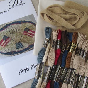 May include: A punch needle pattern kit with the text "1876 Flag". The kit includes a pattern, fabric, thread, and a beige wool strip. The pattern features two American flags and the year 1876.