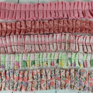 May include: Close-up of five strips of ruffled fabric in various pink and patterned designs. The fabrics include solid pink, floral, plaid, and patterned prints. Each strip is approximately 1 inch wide.