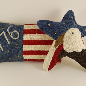 May include: Two patriotic throw pillows. One is rectangular with a blue field featuring the text "1776" and a red and white striped section. The other is a blue star-shaped pillow with an eagle design.
