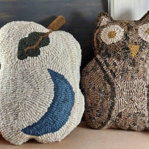 May include: Two decorative, textured pillows. One is shaped like a pear with a green leaf and blue crescent. The other is an owl with large, round eyes. Both pillows are made with a looped, rug-like texture, in neutral and brown tones.
