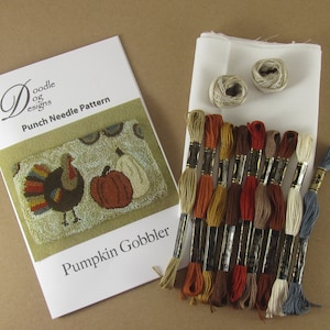 May include: A craft kit for punch needle embroidery featuring a "Pumpkin Gobbler" design. The kit includes a pattern booklet, fabric, thread spools, and a variety of colorful embroidery floss in shades of orange, brown, and cream.