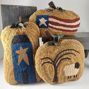 May include: Three decorative, handmade pumpkin-shaped pillows. One features a blue and gold star, another a red and white striped design, and the third a tree and sheep. Each has a brown stem and green leaf accents.