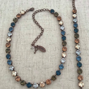 May include: A copper-toned necklace and bracelet set with a gradient of blue, green, and brown crystals. The necklace has a small key charm with the word "Antik" on it.