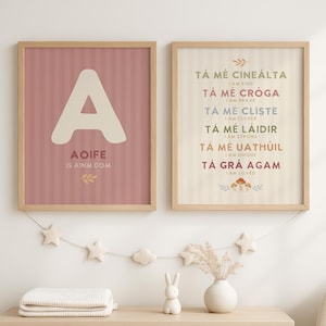 Op de afbeelding: Twee ingelijste wandposters met lichte houten lijsten. De linker poster toont een grote letter A, de tekst AOIFE IS AINM DOM en een blaadje. De rechter poster bevat Ierse zinnen met Engelse vertalingen, waaronder TÁ MÉ CINEÁLTA, TÁ MÉ CRÓGA, TÁ MÉ CLISTE, TÁ MÉ LÁIDIR, TÁ MÉ UATHÚIL en TÁ GRÁ AGAM.