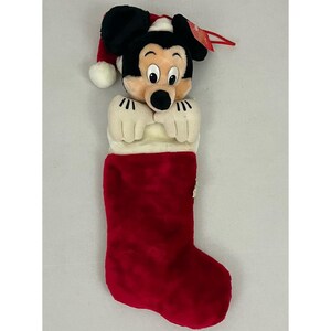 Op de afbeelding: Een rode kerstsok met een Mickey Mouse-figuur van pluche. De sok heeft een witte manchet en een Mickey Mouse-hoofd en -handen van pluche. Mickey draagt een kerstmuts.