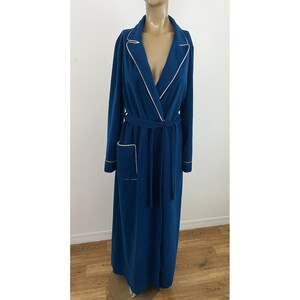 Pode incluir: Robe comprido azul-petróleo com acabamento branco nas lapelas, bolsos e punhos. O robe tem um cinto a condizer e é exibido num manequim. O robe é feito de um material macio.