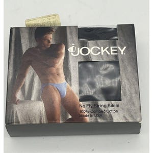 Peut inclure: Un paquet de sous-vêtements noirs Jockey No Fly String Bikini. L'emballage présente un homme en sous-vêtements bleu clair. Le texte sur l'emballage indique "Jockey", "No Fly String Bikini", "100% Combed Cotton" et "Made in USA".