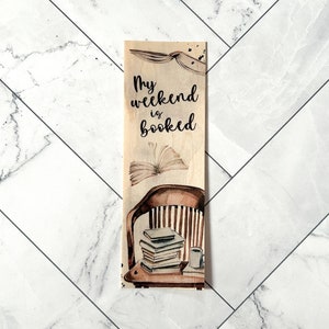 May include: Wooden bookmark with a brown and white striped chair, a stack of books, a cup of coffee, and the text "My weekend is booked".