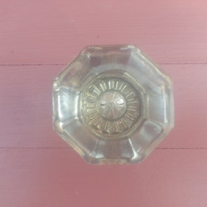 May include: A clear glass door knob with a decorative, octagonal shape and a star-shaped design in the center.