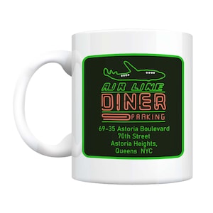 May include: White ceramic mug with a green and black design featuring a plane, the text "AIR LINE DINER", and the address "69-35 Astoria Boulevard, 70th Street, Astoria Heights, Queens NYC".