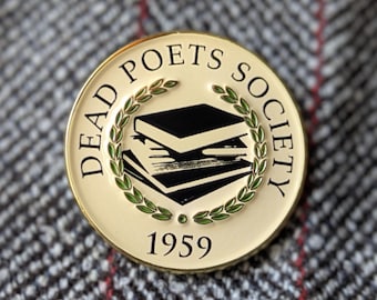Può includere: Uno spillo dorato con sfondo bianco e dettagli neri e verdi. Lo spillo presenta una ghirlanda di foglie verdi che circonda una pila di libri. Il testo "DEAD POETS SOCIETY" è scritto attorno alla ghirlanda, e l'anno "1959" è scritto sotto la ghirlanda.
