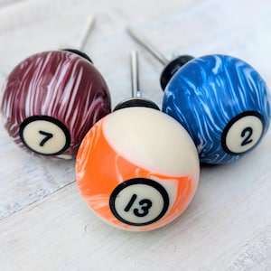 May include: A white ceramic mug with a black handle and the text "But First, Coffee" in a bold, black font. The mug is set against a blurred background, suggesting a cosy setting.