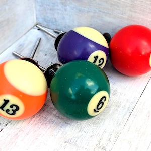 May include: Four spherical cabinet knobs designed to resemble billiard balls. The set includes an orange ball with the number 13, a purple ball with the number 12, a dark green ball with the number 6, and a red ball with the number 3. Each knob features a metal mounting bolt.