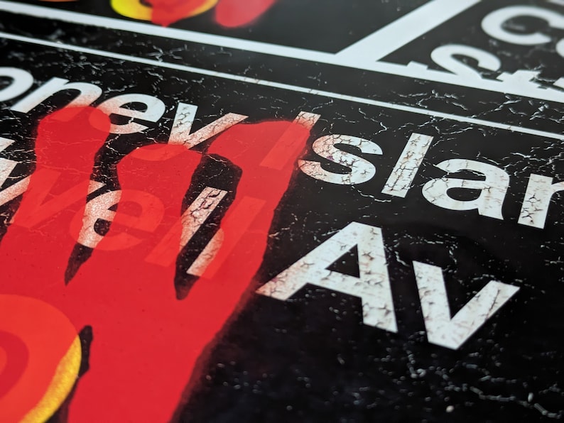 Op de afbeelding: Een zwart-wit bord met de woorden "Cornell Island Av" in witte letters. Het bord is verweerd en heeft een rode handafdruk aan de linkerkant.