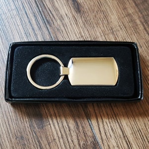 May include: A silver key chain with a blank rectangular tag. The keychain is in a black velvet box.