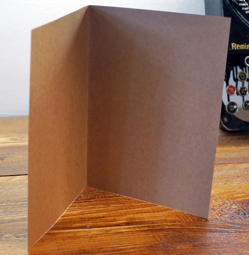 May include: A blank brown card with a folded edge. The card is sitting on a wooden surface.