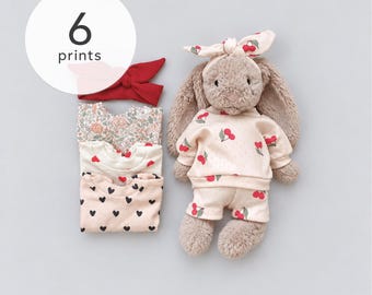 May include: A plush brown rabbit toy wearing a cream-colored sweatshirt and shorts with a red cherry print and a matching headband. Beside it are three folded shirts with floral, heart, and cherry patterns, plus a solid red headband. Text reads 6 prints.