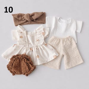 May include: A set of baby clothing including a brown knotted headband, a white short-sleeved top with a small bird print and ruffled shoulders, a pair of brown ruffled bloomers, and a white short-sleeved shirt with matching beige trousers.