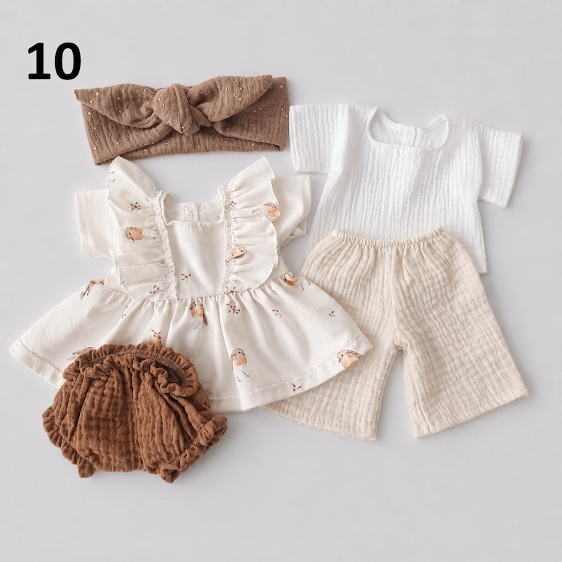 May include: A set of baby clothing including a brown knotted headband, a white short-sleeved top with a small bird print and ruffled shoulders, a pair of brown ruffled bloomers, and a white short-sleeved shirt with matching beige trousers.