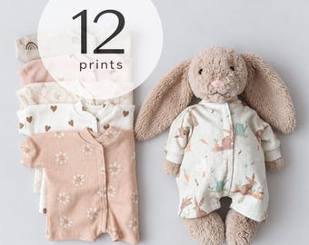 May include: A stack of baby onesies featuring 12 prints and a plush stuffed rabbit toy wearing a matching onesie with a rabbit, carrot, and watering can pattern. The onesies include various colors and designs like flowers, hearts, and rainbows.