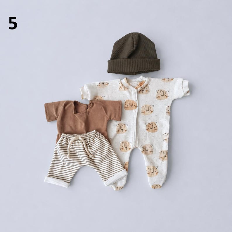 May include: A set of baby clothing including a dark olive green beanie, a solid brown short-sleeve shirt, white and brown striped shorts with a drawstring waist, and a white footed sleeper featuring a repeating brown tiger face pattern.