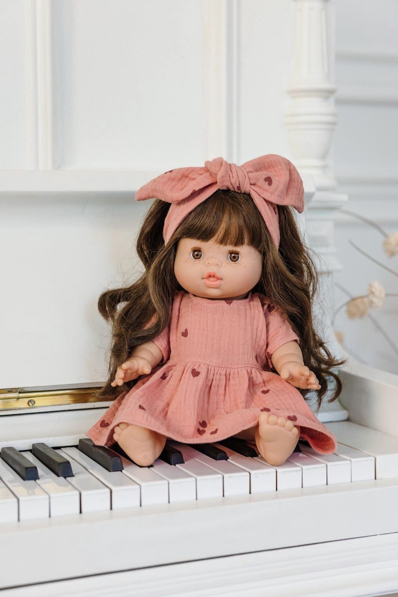 A Paola Reina doll dress for Minikane gordis doll - old rose with dark heart patterns and a matching headband.