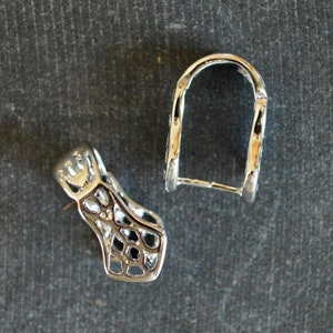 May include: Two silver metal jewelry clasps. One clasp is a simple loop, the other is a more ornate design with a geometric pattern.