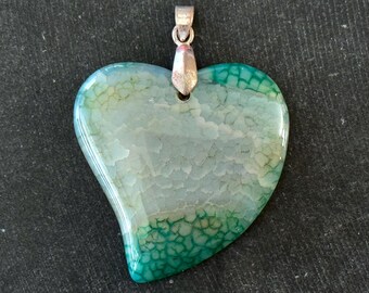 Puede incluir: Un colgante en forma de corazón hecho de ágata verde y blanca con un aro de plata.