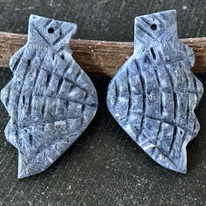 May include: A pair of gray and white ceramic earrings with a textured, geometric design. The earrings have a hole at the top for hanging.