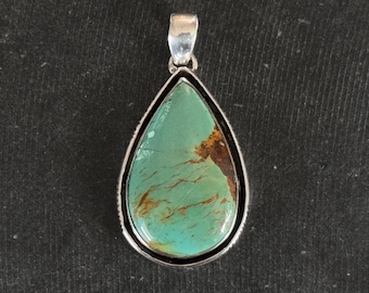 May include: Teardrop-shaped turquoise pendant with a silver-coloured bail and bezel. The turquoise stone has a mottled pattern of blue-green and brown hues. The pendant is displayed against a dark background.